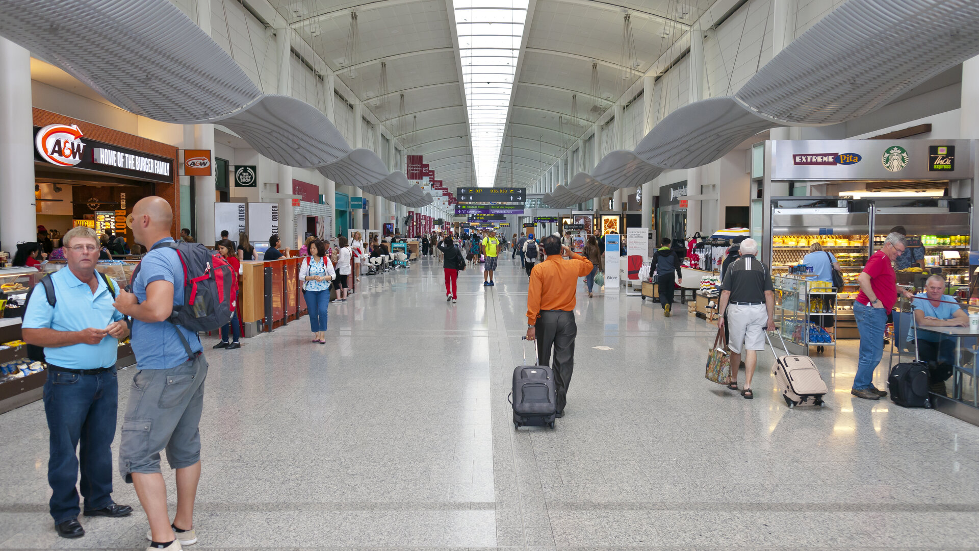 Travellers walking with luggage through the Terminal 1 concourse at Toronto Pearson International Airport.