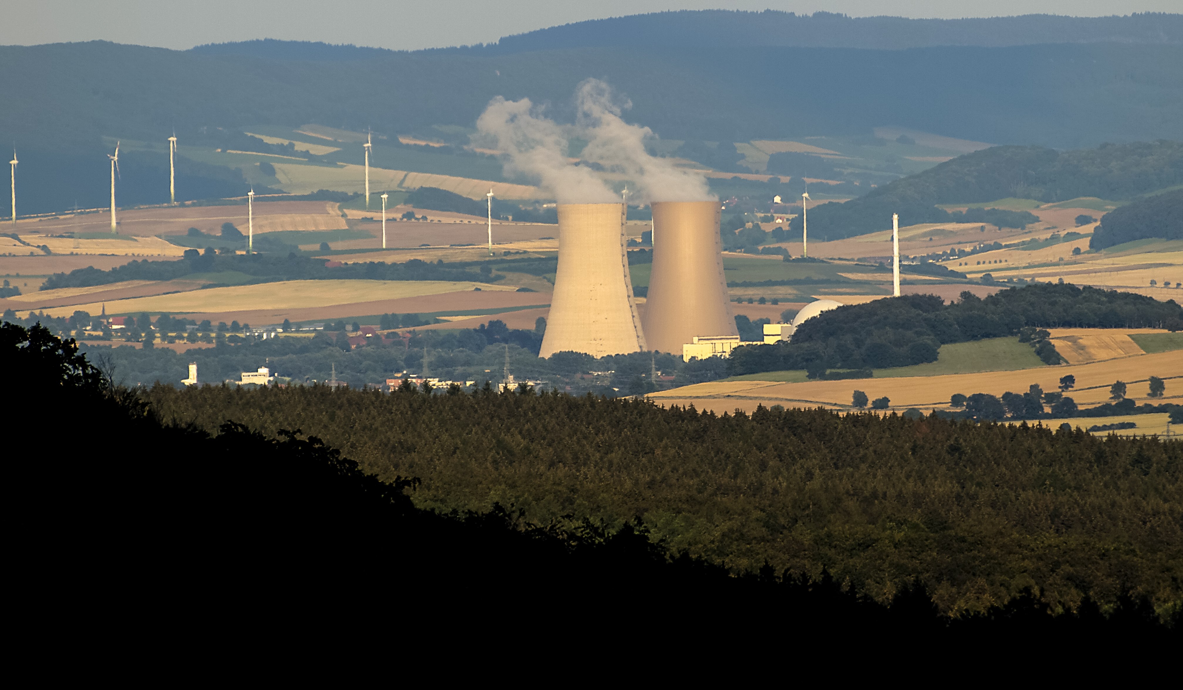 Grohnde nuclear power plant cooling towers with wind turbines visible across rolling farmland hills in Lower Saxony, Germany