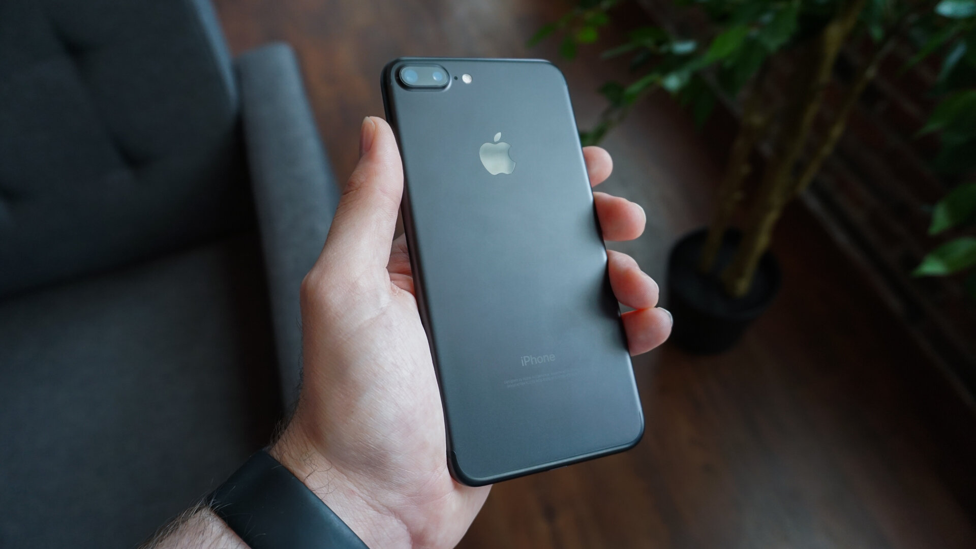 A hand holding a black smartphone, the Apple logo and "iPhone" wordmark visible on the back.