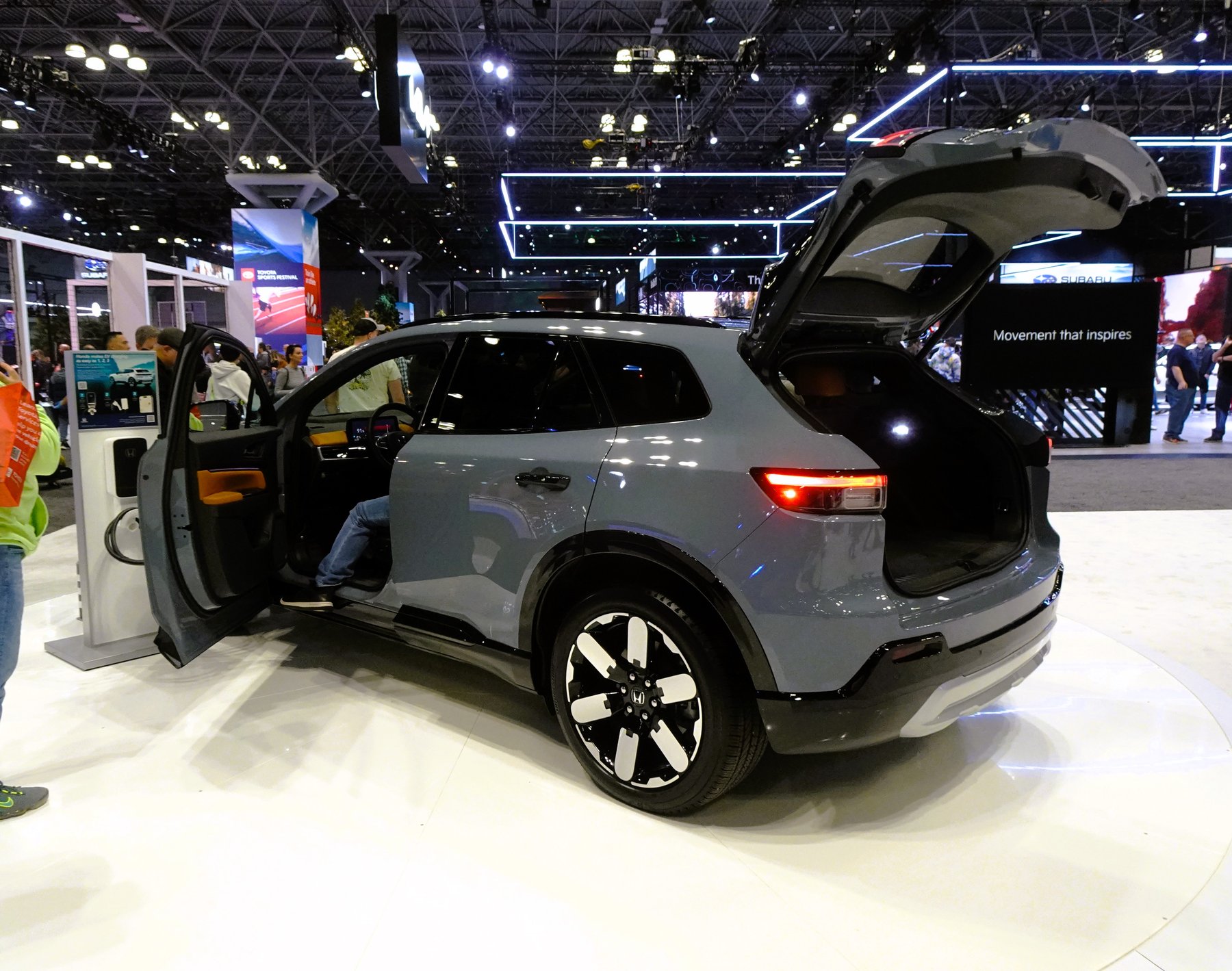 A grey Honda Prologue electric SUV displayed at an auto show with its hatch and door open, against a Honda 'Movement that inspires' branded backdrop.