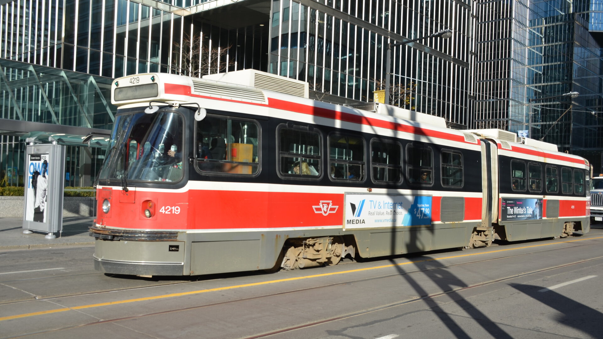 A TTC streetcar stopped in mixed traffic on a downtown Toronto street, with a car visible alongside it.